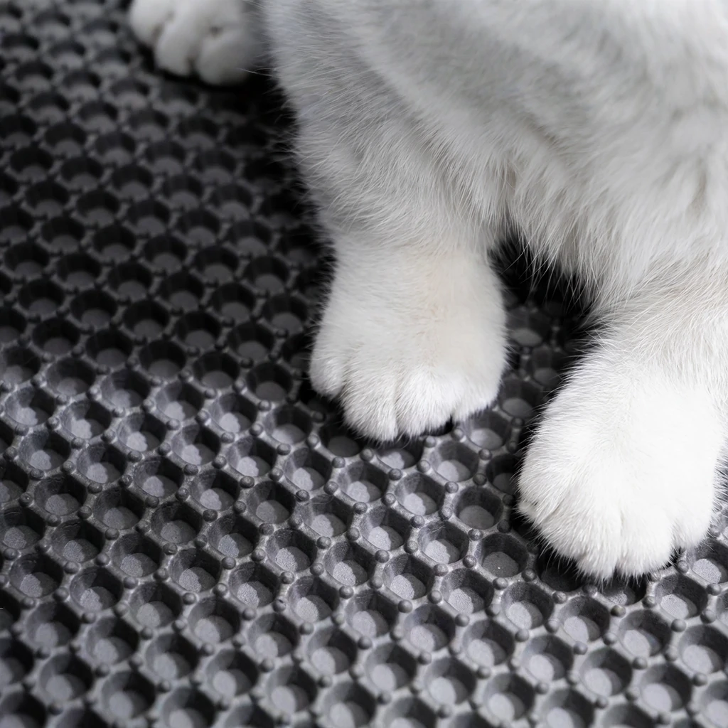 Soft white cat paws rest gently on a charcoal double-layer litter trapping mat with a textured honeycomb design, supporting harmonious pet living in a calm, minimalist space.